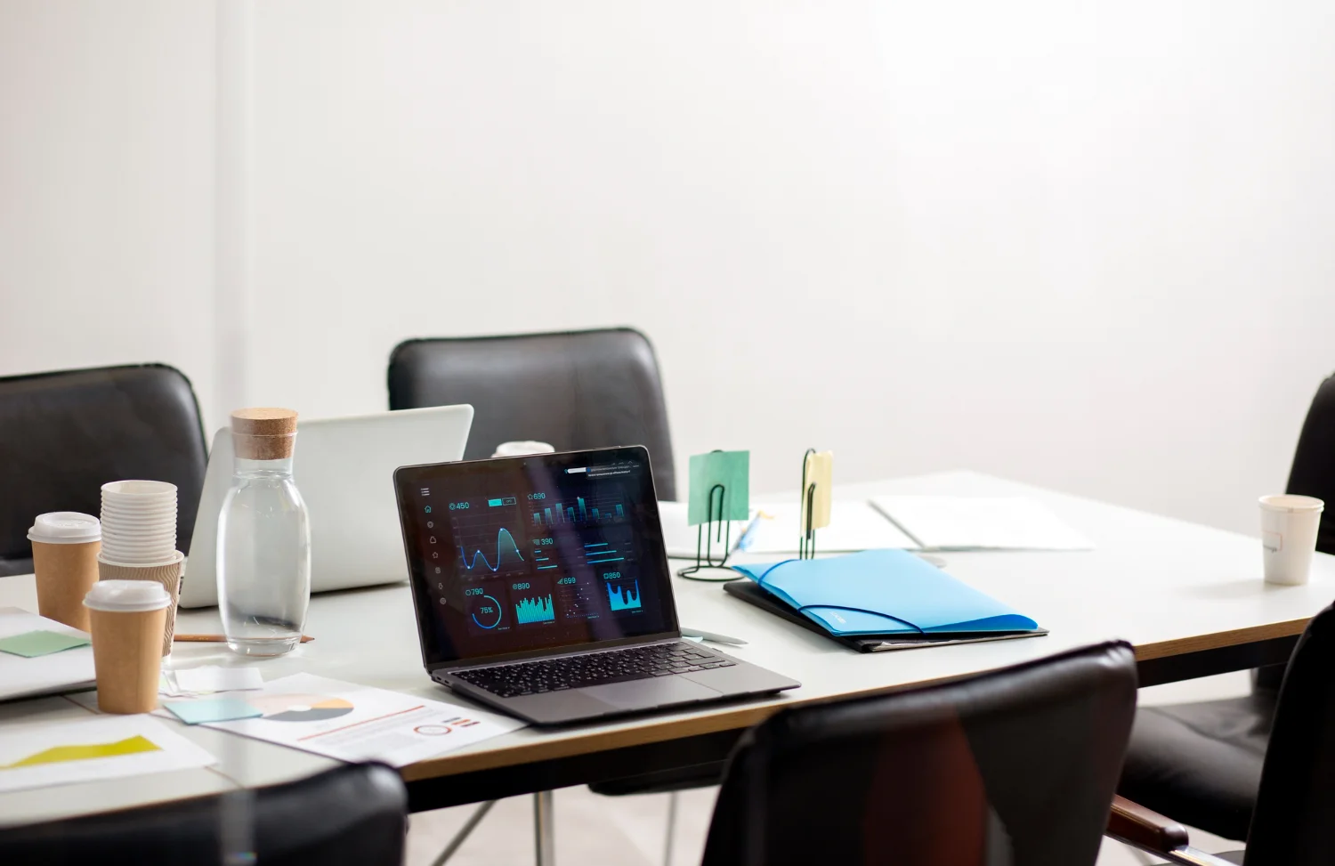 Borderless Recruit office meeting room with a laptop displaying graphs, papers, coffee cups, and a water bottle on a white table.
