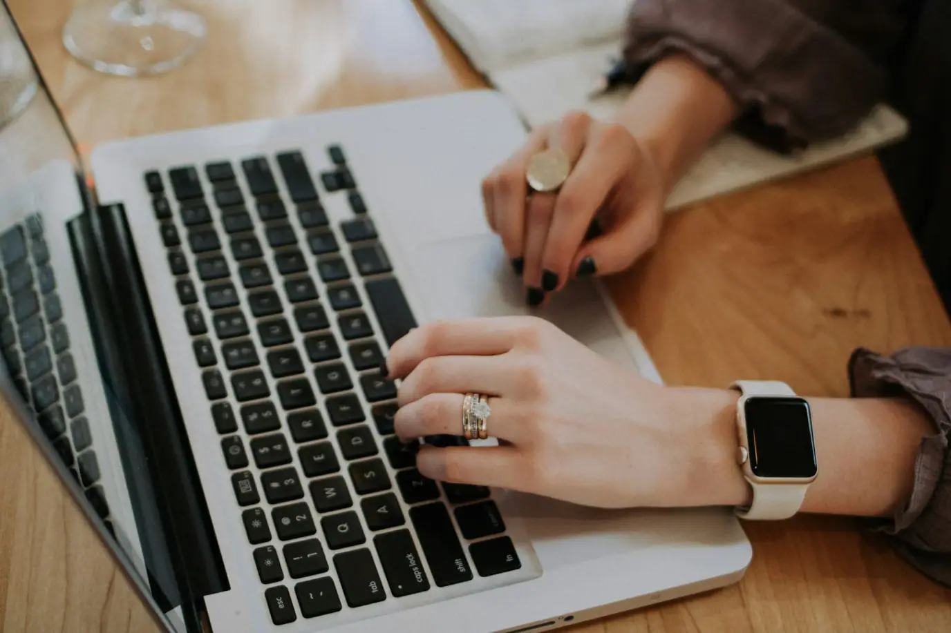 Virtual worker's hands typing on a laptop with a smartwatch on the wrist.