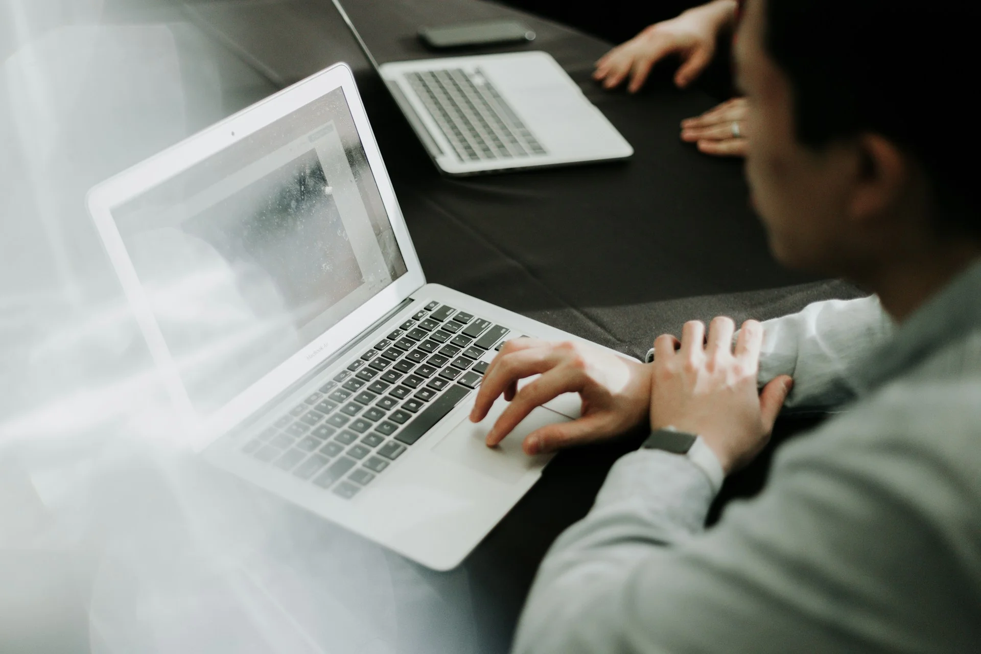 Virtual worker working on a laptop at a dark table with another laptop in the background.